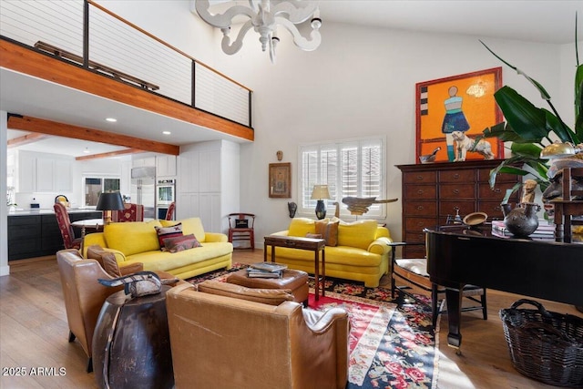 living room featuring beamed ceiling, a notable chandelier, light wood-type flooring, and a high ceiling