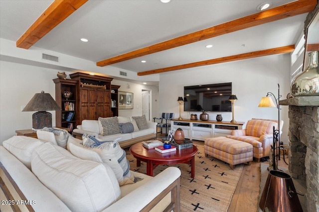 living room with beam ceiling, a stone fireplace, and hardwood / wood-style floors