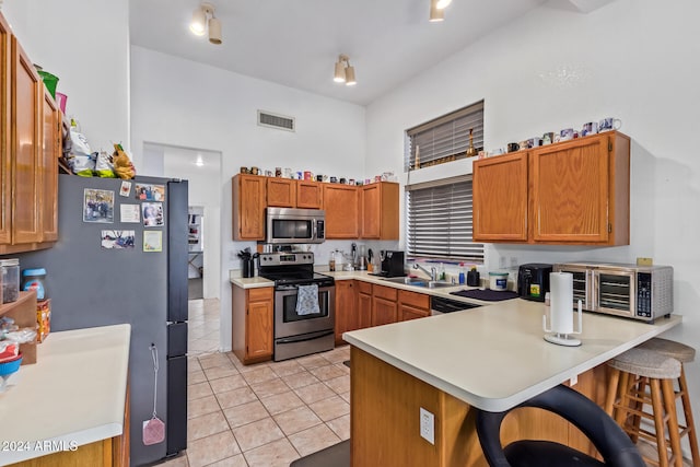 kitchen with stainless steel appliances, kitchen peninsula, light tile patterned floors, sink, and a breakfast bar