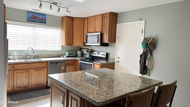 kitchen with a breakfast bar, sink, dark stone countertops, appliances with stainless steel finishes, and a kitchen island