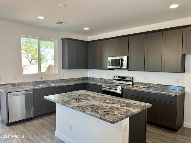 kitchen with dark stone counters, a kitchen island, stainless steel appliances, light hardwood / wood-style flooring, and sink