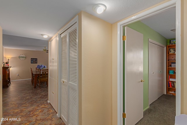 hallway featuring dark colored carpet and a textured ceiling