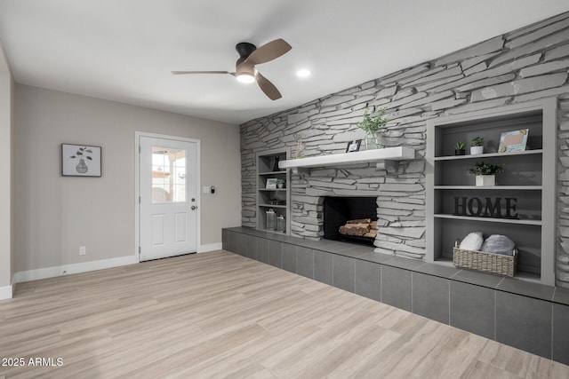 unfurnished living room featuring ceiling fan, built in shelves, a tiled fireplace, and light wood-type flooring