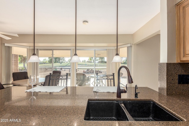 kitchen featuring plenty of natural light, dark stone countertops, a sink, and decorative light fixtures