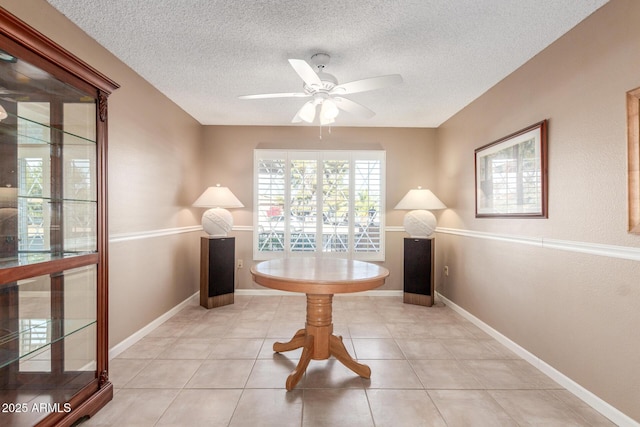 interior space with baseboards, a ceiling fan, a textured ceiling, and light tile patterned flooring