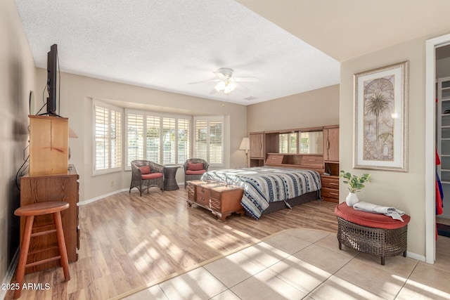 bedroom featuring baseboards, ceiling fan, light wood-style flooring, and a textured ceiling