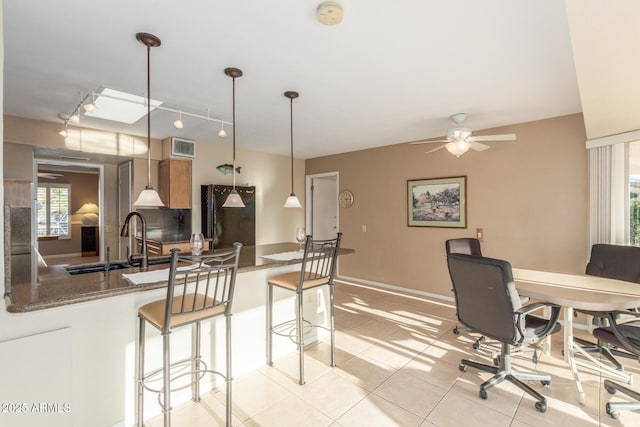 kitchen featuring decorative light fixtures, freestanding refrigerator, a sink, dark stone counters, and a peninsula