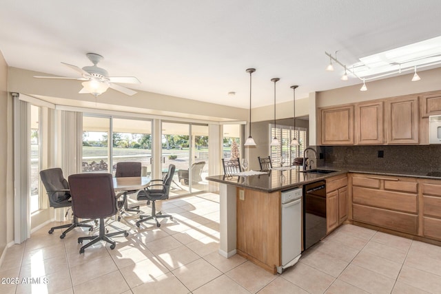 kitchen featuring decorative light fixtures, a sink, dark stone countertops, dishwasher, and a peninsula