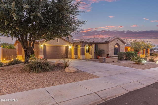 mediterranean / spanish-style home with fence, a tile roof, stucco siding, a garage, and driveway