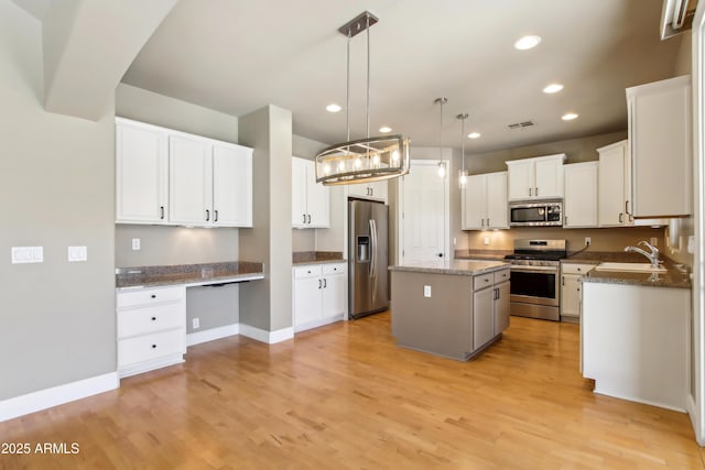 kitchen with light wood-style flooring, a sink, stainless steel appliances, white cabinetry, and a center island