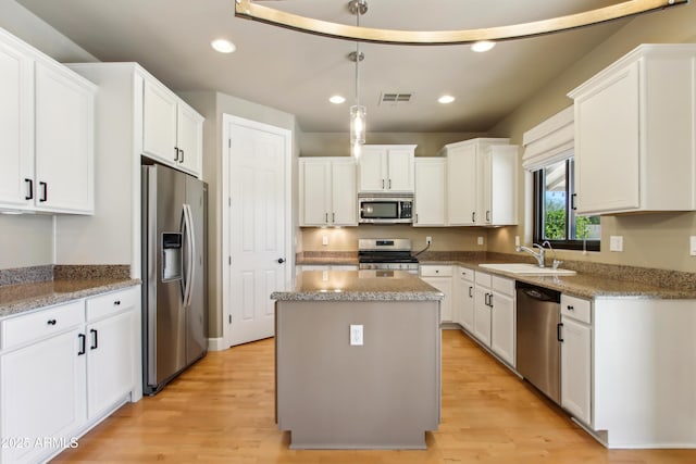 kitchen featuring white cabinets, appliances with stainless steel finishes, a kitchen island, and a sink