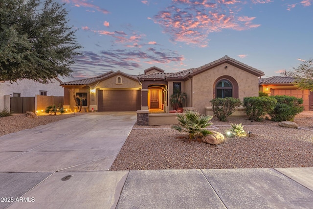 mediterranean / spanish house featuring fence, a tiled roof, stucco siding, a garage, and driveway