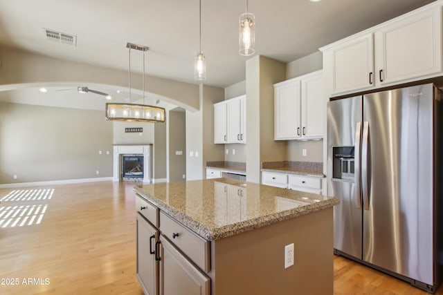 kitchen with visible vents, a center island, ceiling fan, a fireplace, and stainless steel refrigerator with ice dispenser