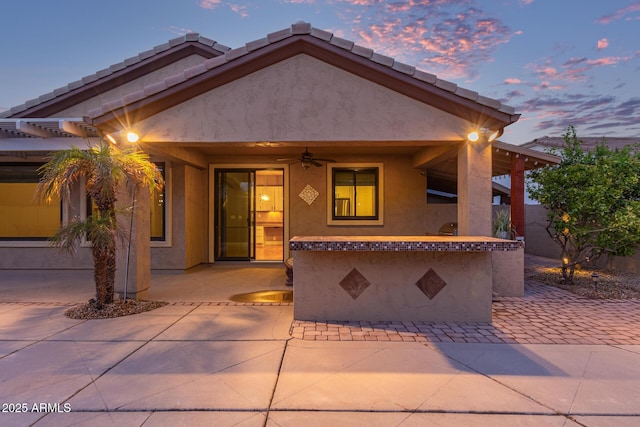 view of front of home featuring stucco siding, a patio, ceiling fan, and a tile roof