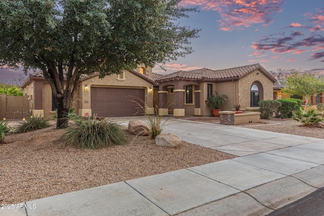 mediterranean / spanish house featuring stucco siding, fence, concrete driveway, a garage, and a tiled roof