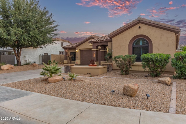 mediterranean / spanish home featuring stucco siding, fence, concrete driveway, and a tile roof