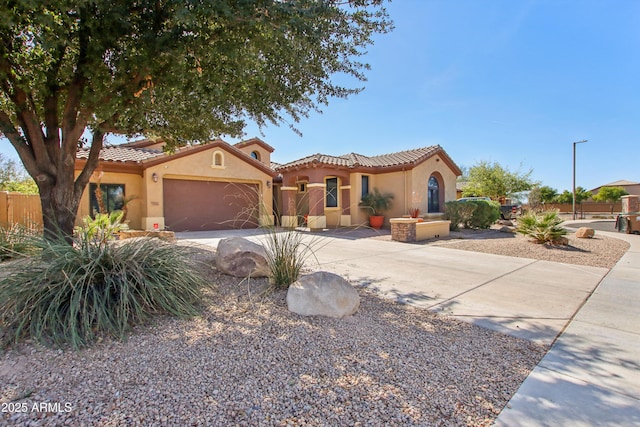 mediterranean / spanish house featuring fence, a tile roof, concrete driveway, stucco siding, and a garage