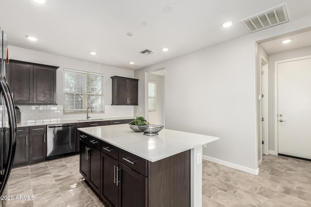 kitchen featuring dark brown cabinetry, sink, backsplash, a kitchen island, and appliances with stainless steel finishes