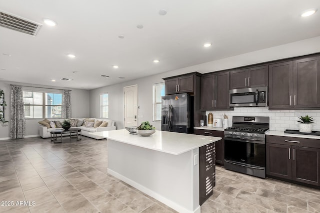 kitchen with dark brown cabinetry, decorative backsplash, a center island, and appliances with stainless steel finishes