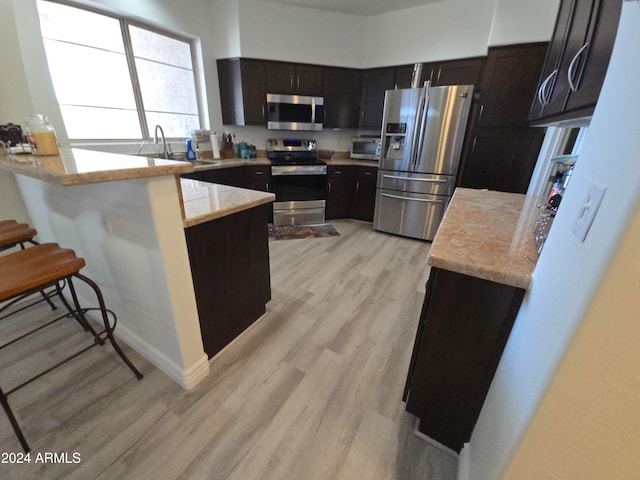 kitchen featuring sink, appliances with stainless steel finishes, light hardwood / wood-style floors, kitchen peninsula, and a breakfast bar area