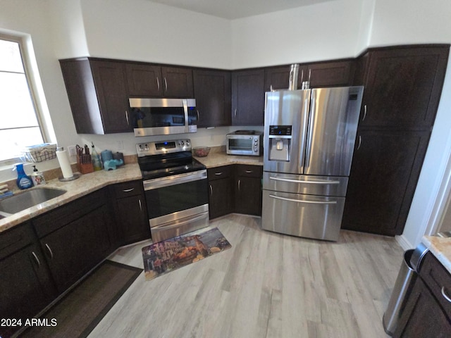 kitchen with dark brown cabinetry, stainless steel appliances, light hardwood / wood-style flooring, and sink