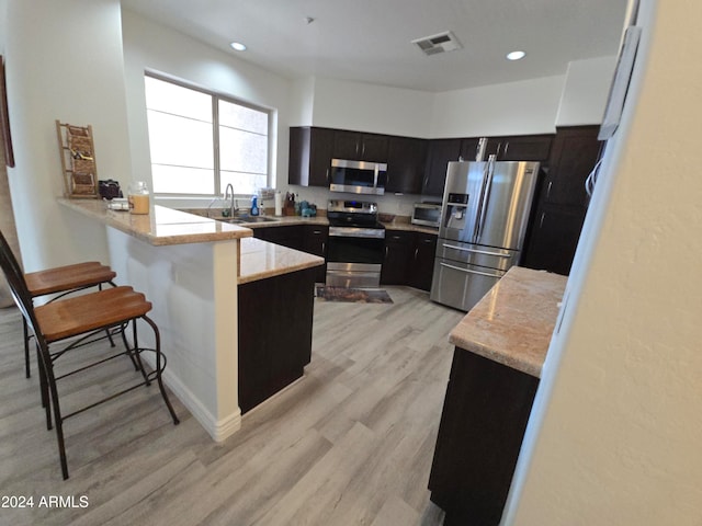 kitchen featuring sink, a kitchen breakfast bar, light hardwood / wood-style flooring, kitchen peninsula, and appliances with stainless steel finishes