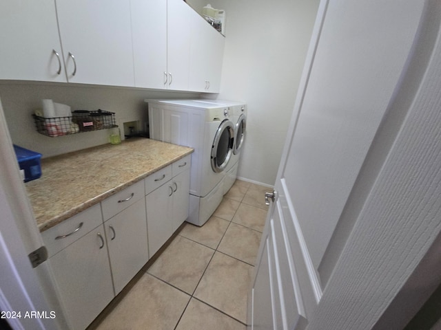 laundry room with washing machine and clothes dryer, light tile patterned floors, and cabinets