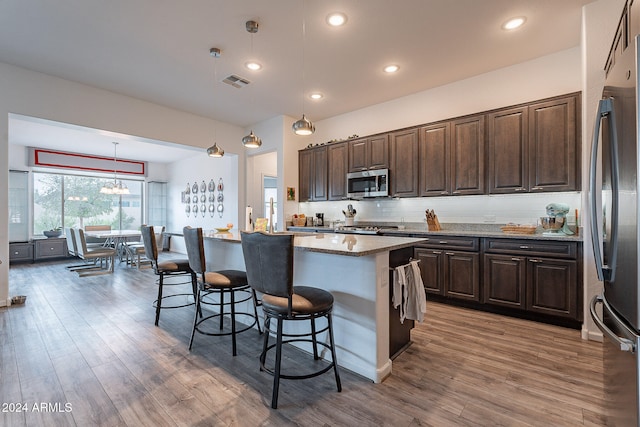 kitchen with stainless steel appliances, wood-type flooring, decorative light fixtures, and a kitchen island