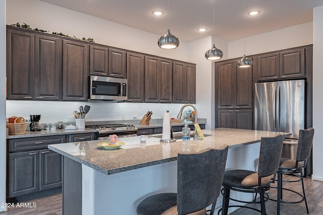 kitchen featuring a center island with sink, pendant lighting, dark wood-type flooring, and stainless steel appliances