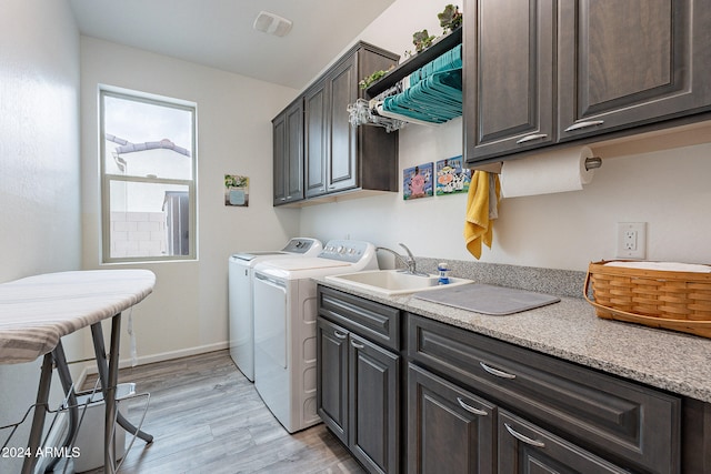 clothes washing area with light hardwood / wood-style floors, cabinets, sink, and separate washer and dryer