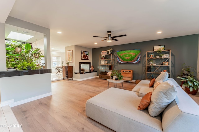 living room with a multi sided fireplace, a skylight, ceiling fan, and light wood-type flooring