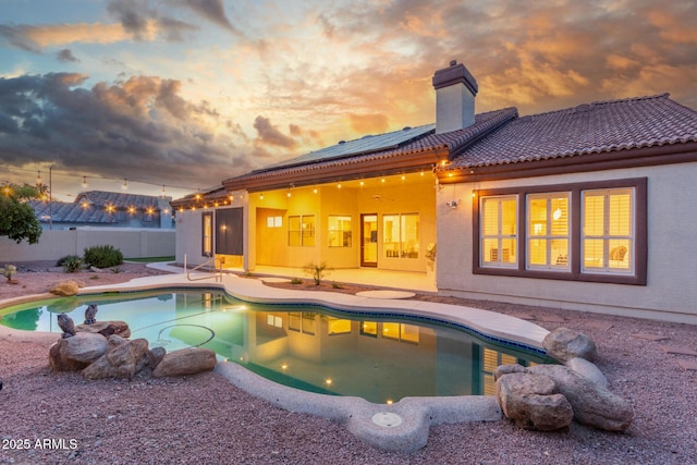 back of house at dusk with a chimney, a patio area, a fenced in pool, a fenced backyard, and stucco siding