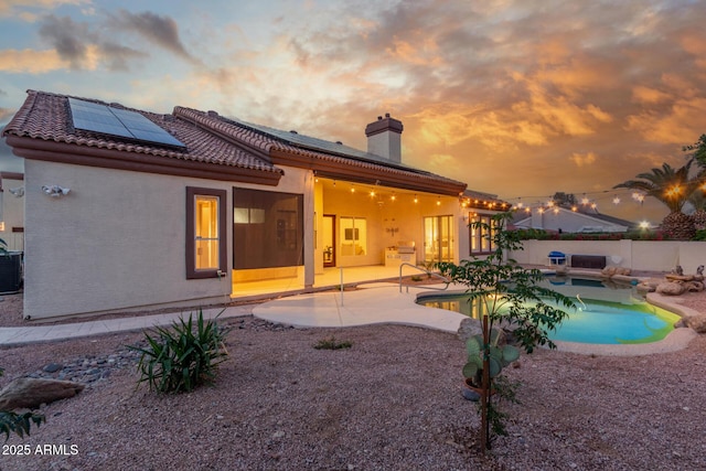 rear view of house with a fenced in pool, a chimney, solar panels, and a patio area