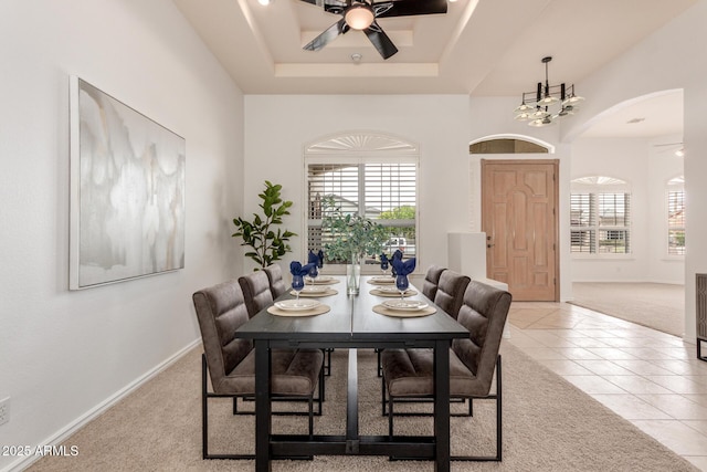 carpeted dining space with a ceiling fan, arched walkways, baseboards, tile patterned floors, and a tray ceiling