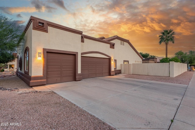 view of side of home featuring an attached garage, concrete driveway, stucco siding, and fence