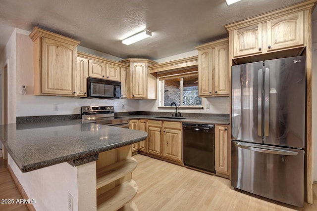 kitchen featuring light wood finished floors, light brown cabinetry, a sink, a peninsula, and black appliances