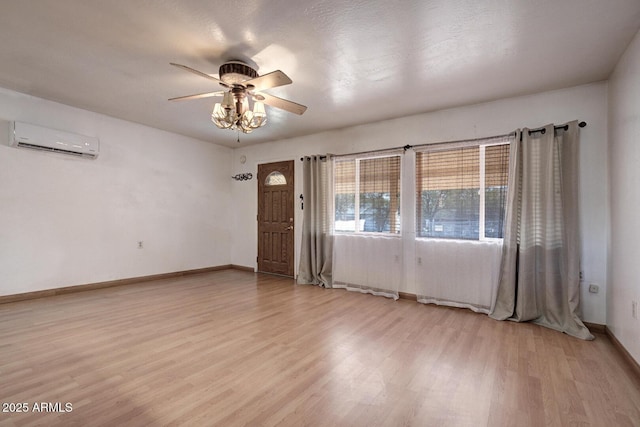 interior space featuring baseboards, an AC wall unit, ceiling fan, and light wood-style floors