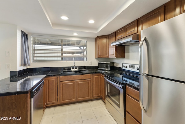 kitchen with a sink, under cabinet range hood, light tile patterned floors, tile countertops, and appliances with stainless steel finishes