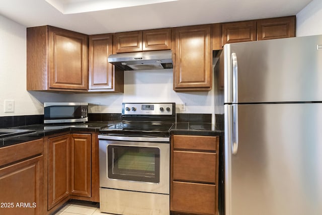 kitchen with stainless steel appliances, tile counters, under cabinet range hood, and brown cabinets