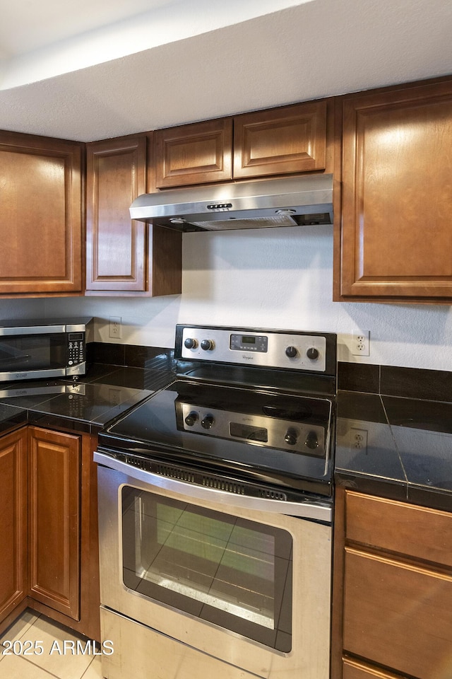 kitchen featuring tile countertops, brown cabinets, appliances with stainless steel finishes, and under cabinet range hood