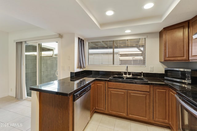 kitchen featuring a sink, light tile patterned floors, brown cabinetry, a peninsula, and appliances with stainless steel finishes