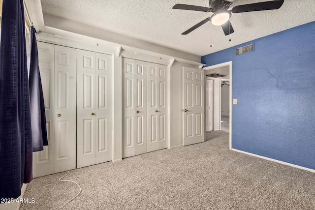 unfurnished bedroom featuring ceiling fan, a textured ceiling, carpet floors, and two closets