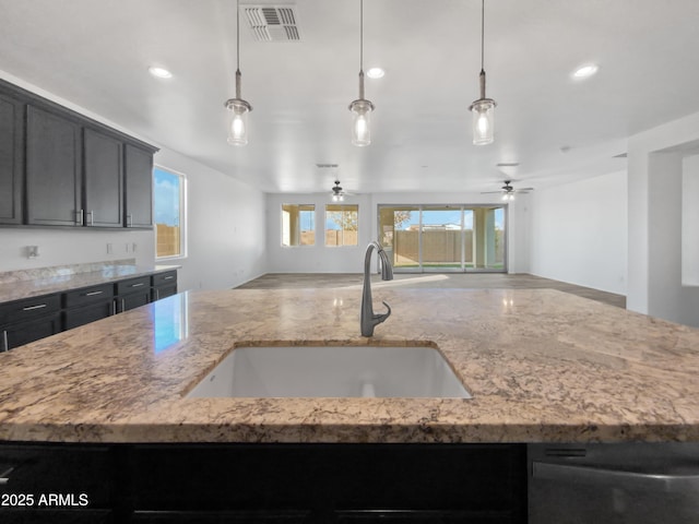 kitchen featuring pendant lighting, sink, a kitchen island with sink, and light stone countertops