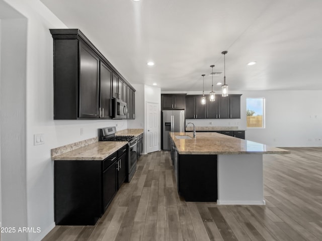 kitchen featuring stainless steel appliances, pendant lighting, hardwood / wood-style flooring, and a center island with sink