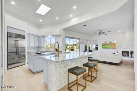 kitchen featuring ceiling fan, a skylight, a kitchen island, built in refrigerator, and light wood-type flooring