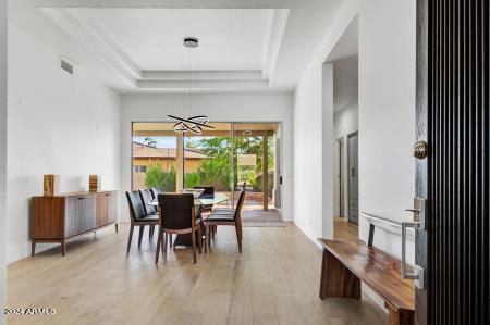 dining area with light hardwood / wood-style flooring, a tray ceiling, and a notable chandelier