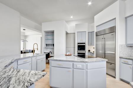 kitchen featuring appliances with stainless steel finishes, decorative backsplash, light stone countertops, a center island, and sink