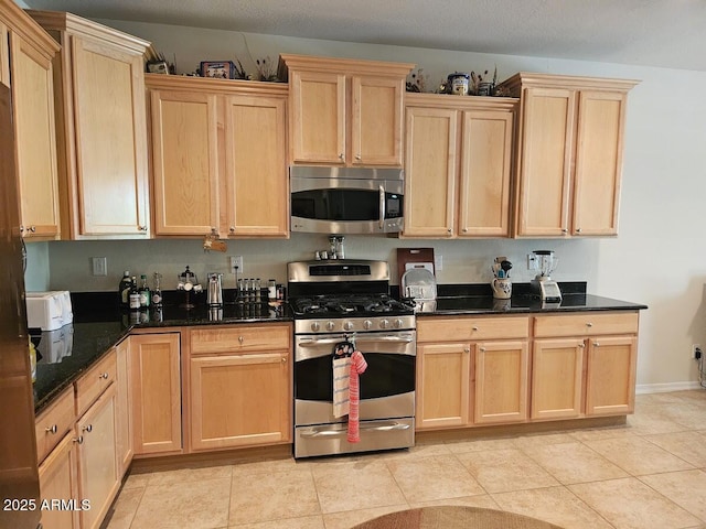 kitchen with dark stone counters, appliances with stainless steel finishes, and light brown cabinets