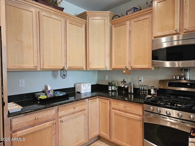 kitchen featuring stainless steel appliances, dark stone countertops, and light brown cabinets