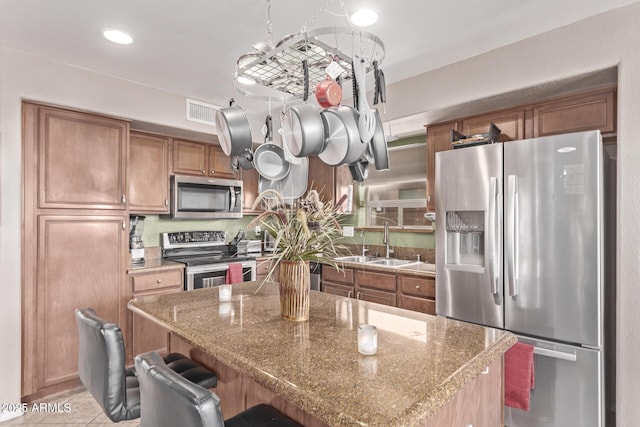 kitchen with a kitchen bar, visible vents, a sink, stainless steel appliances, and brown cabinetry